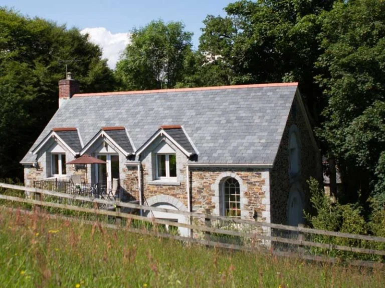 Exterior shot of Higher Hill Cottage at Bosinver, surrounded by trees and a field.