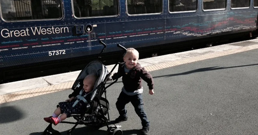 Child with a pram smiling at the camera waiting for a train in Cornwall.