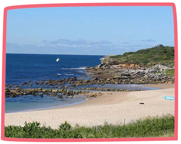 Wide shot of a sandy beach in Cornwall on a sunny day with a boat in the distance.