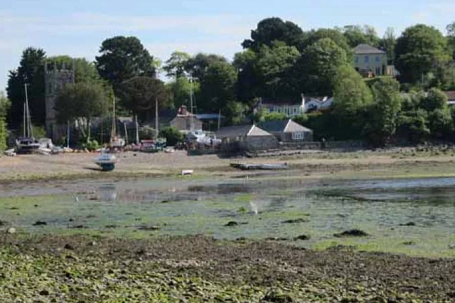 Boats beached by Helford River next to a church on a sunny day.