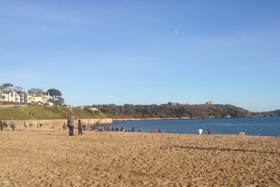 Group of people on Falmouth beach on a sunny winter day.