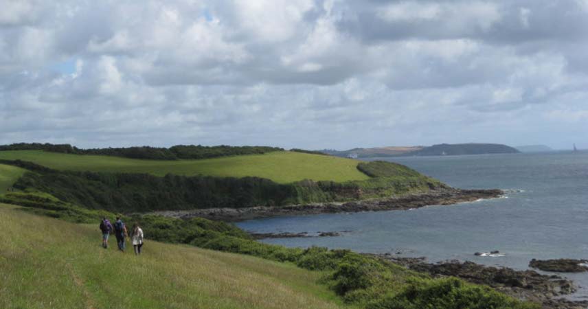 Landscape image showing three people admiring the Cornish coastline with the sea in the distance