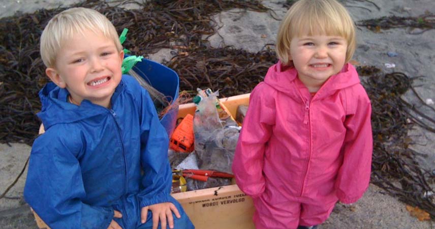 Two toddlers in waterproof onesies posing in front of litter that has been collected from a beach in Cornwall