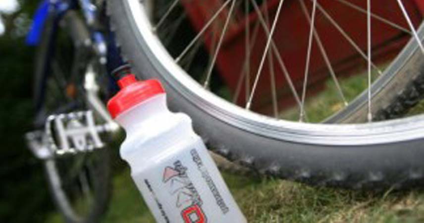 Close up picture of a clear sports bottle with a red lid, there is a bike tyre visible in the background