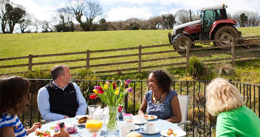 Four people sat around an outside table enjoying food with a field and tractor visible in the background