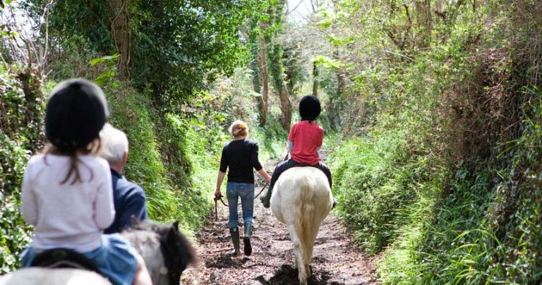 Two children riding ponies being led by adults down a country lane at Bosinver.