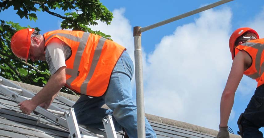 Men in orange hi vis jackets installing solar panels onto the roof of a building