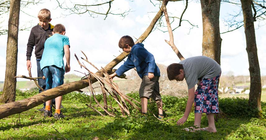 Four children building a den in a field in Cornwall using tree branches