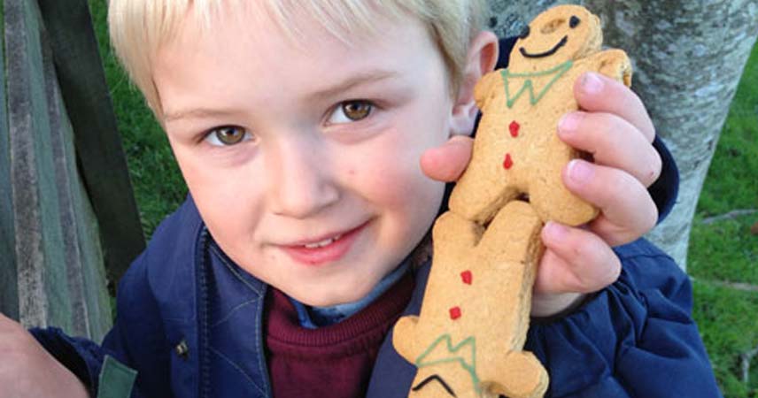 Young boy smiling for the camera holding two gingerbread men that he baked with Pat at Bosinver