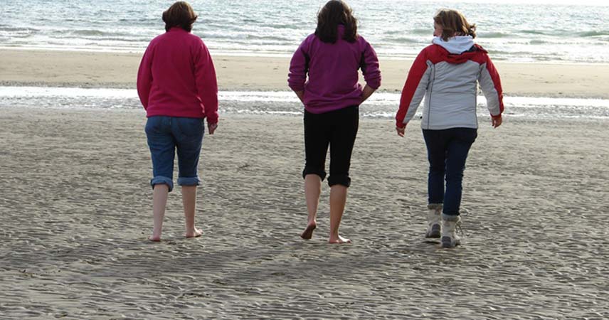 Trio of people walking towards the sea on a beach in Cornwall.