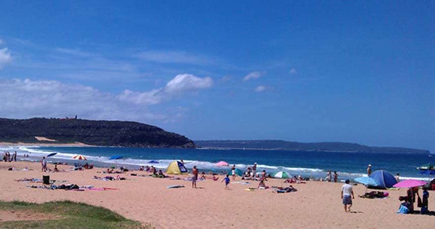 Picture of a beach in summer on a sunny Day. There's a lot of people relaxing on the sand.