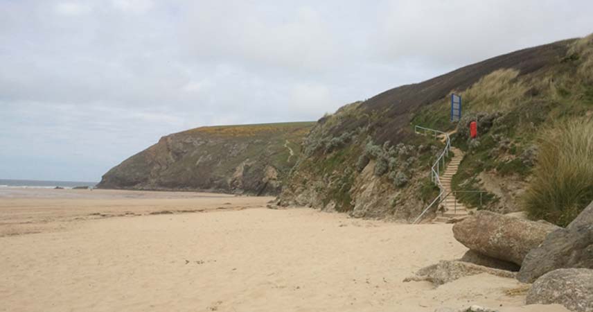 Picture of the beach at Bedruthan on a grey day in Cornwall. Winding steps lead to the coast path.