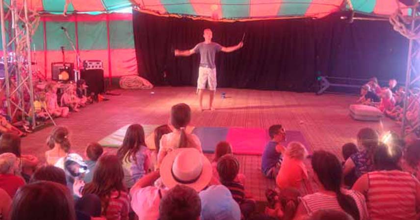 Adult standing in a tent in front of an audience of children at Boscawen Park Truro in Cornwall. Some of the children have their face painted.