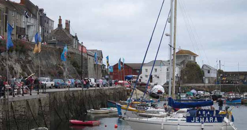 Boats floating in the harbour in Mevagissey in Cornwall. Flags fly in the wind as people walk past.