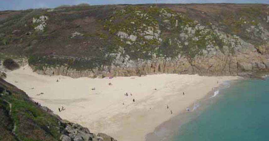 Aerial photo of Porthcurno beach in Cornwall with people relaxing on the sand.