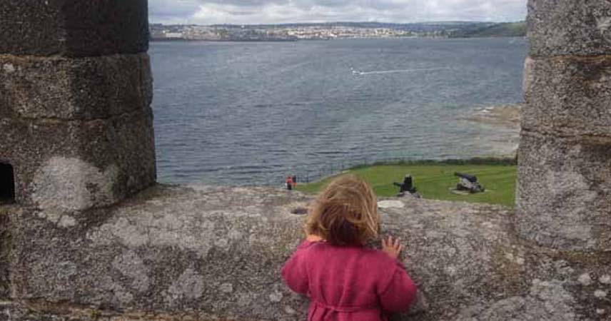 Child looking over a wall at St Mawes in Cornwall, looking out to the water and the boats going passed.