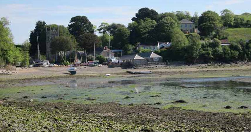 Boats beached by Helford River next to a church on a sunny day.