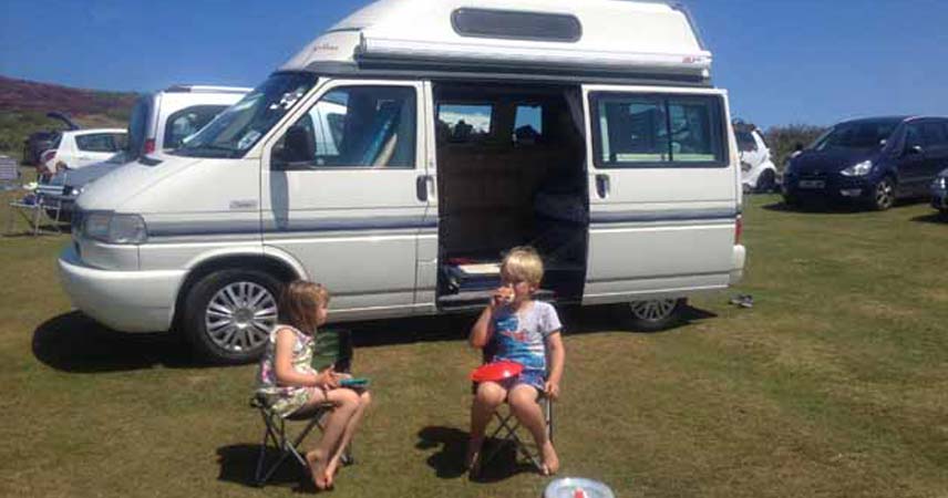 Two children eating lunch outside of a campervan in Godrevy on a sunny day.