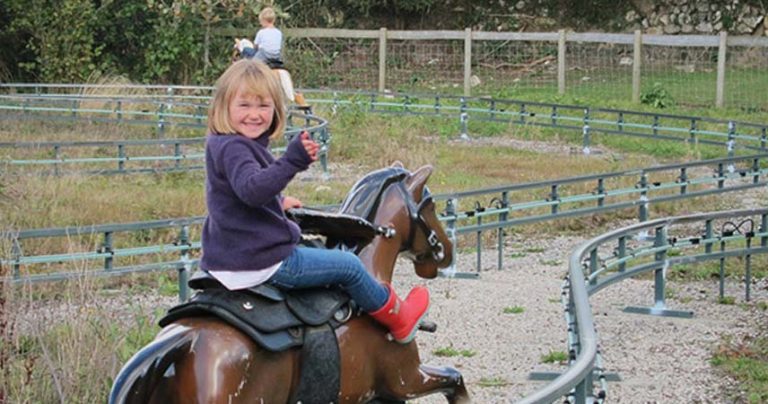 Child smiling at the camera whilst riding a toy horse at Crealy Adventure Park