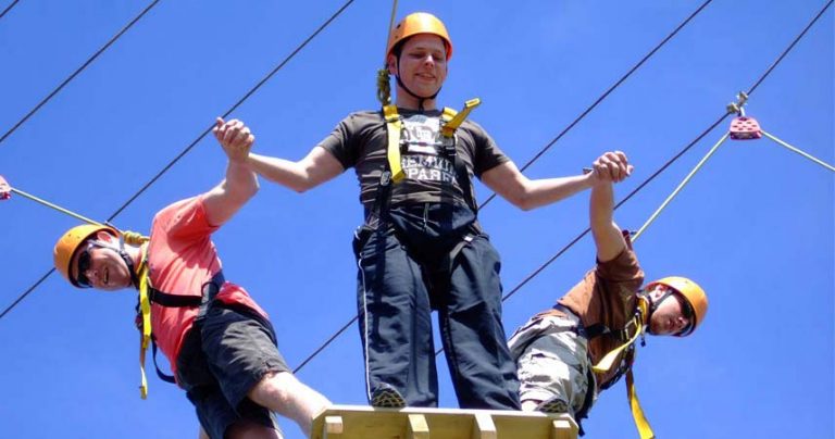 Three men holding hands with protective hard hats on high ropes in Cornwall.