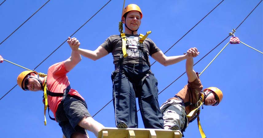 Three men holding hands with protective hard hats on high ropes in Cornwall.