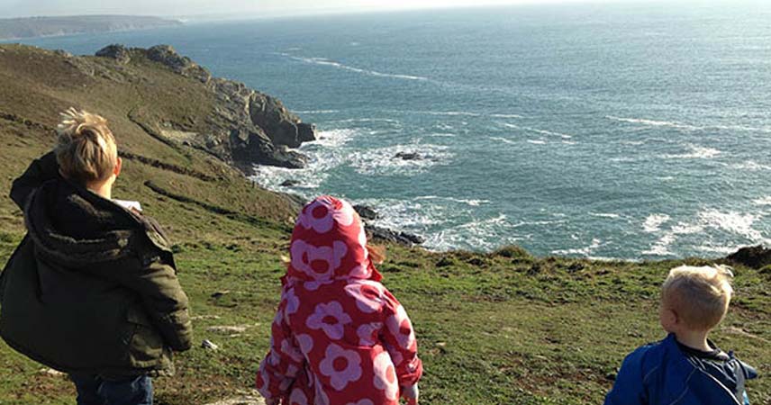 Three children in coats looking out to sea at Prussia Cove.