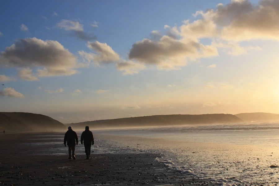 Two people walking along the beach in Cornwall on a sunny winter day.