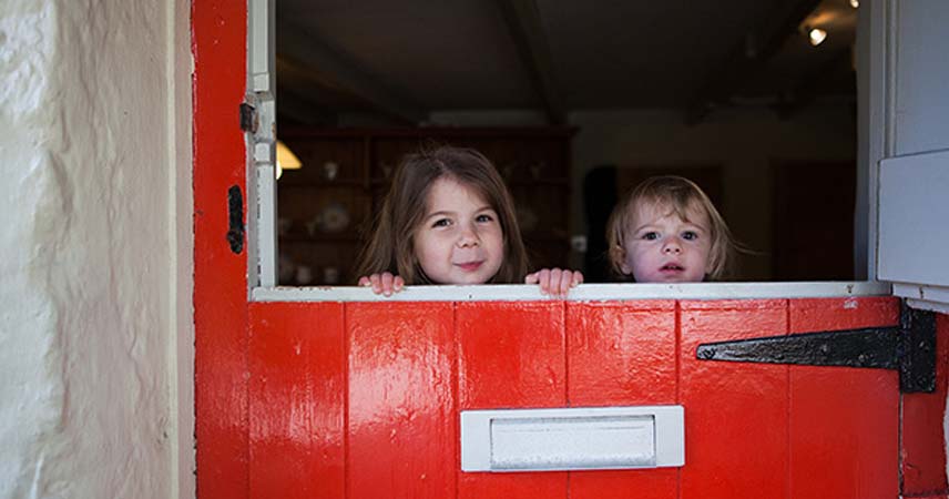 Children peering over a red barn door smiling for the camera.