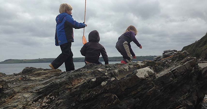 Three children rockpooling on a grey day in Cornwall.