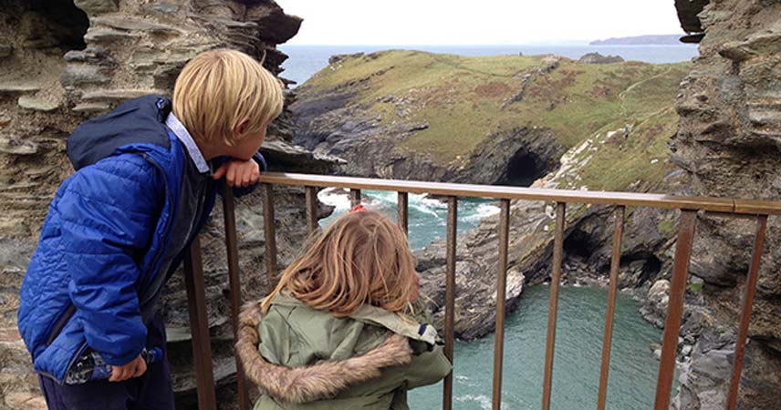 Two children peering over railings at Tintagel Castle in Cornwall.