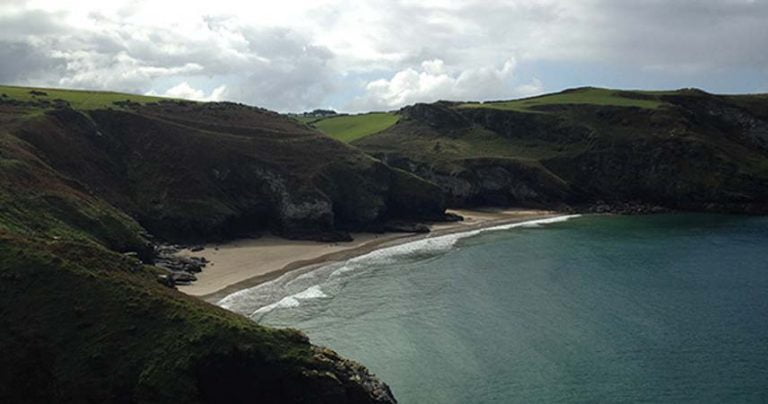 Beach at Tintagel in Cornwall from the air, showcasing the sandy beach, rolling hills and green sea.