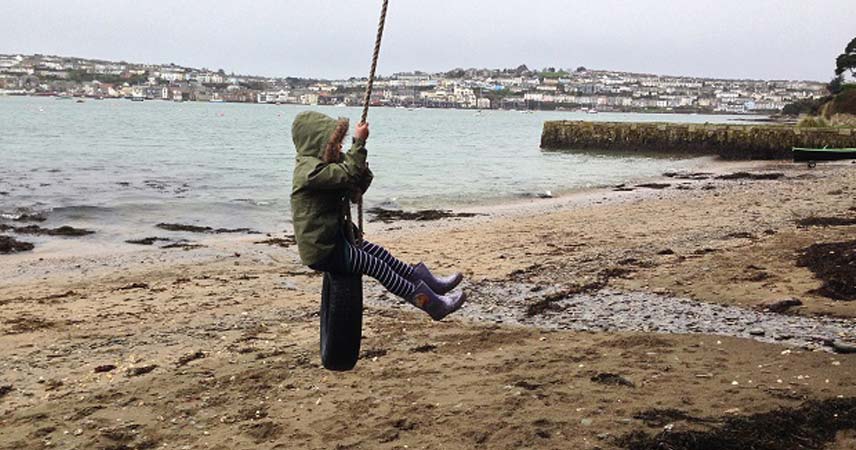 Child on a rope swing in Cornwall, with a coastal town in the background.