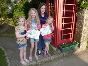 Four girls holding two maps of Bosinver in Cornwall, stood in front of Brittish red phone box