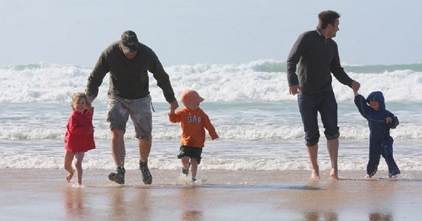 Fathers and children running from the sea on a beach in Cornwall.