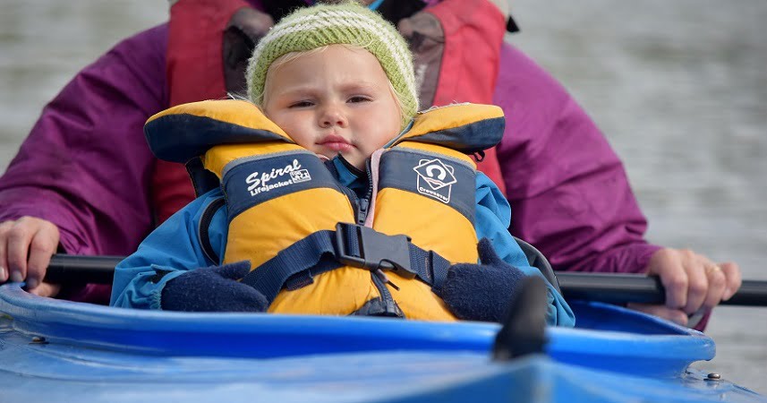 Child in a life jacket with a hat on canoeing down the river