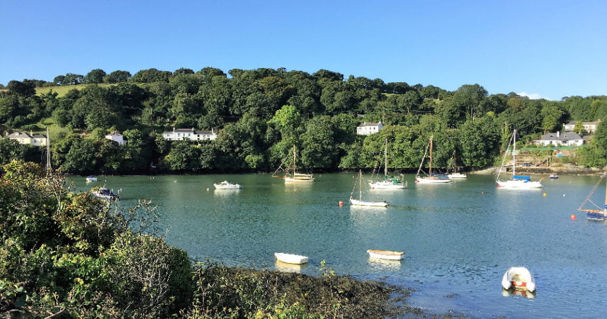 Picture of boats moored on the Fal River with rolling hills and trees in the background.