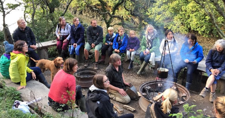 Group of adults and children gathered around an open fire learning about Cornish food.