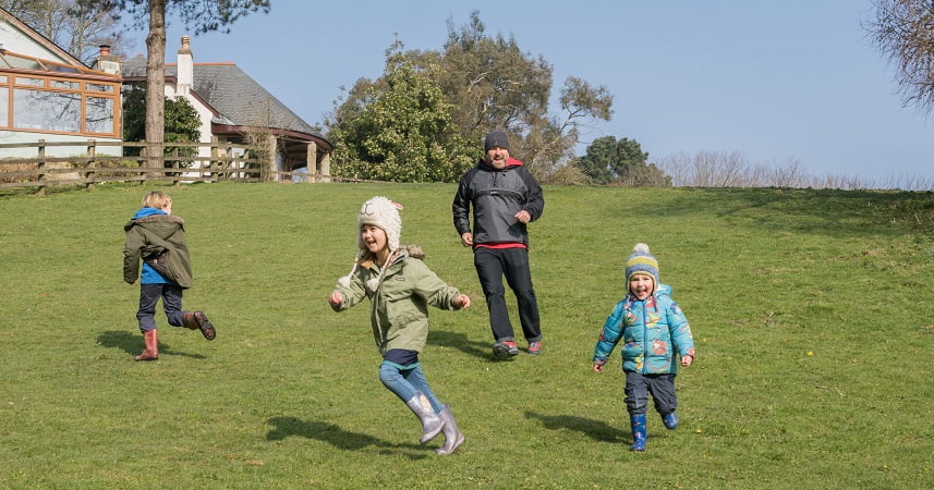 Three children running around Bosinver on a sunny day whilst wrapped up warm in hats and coats.