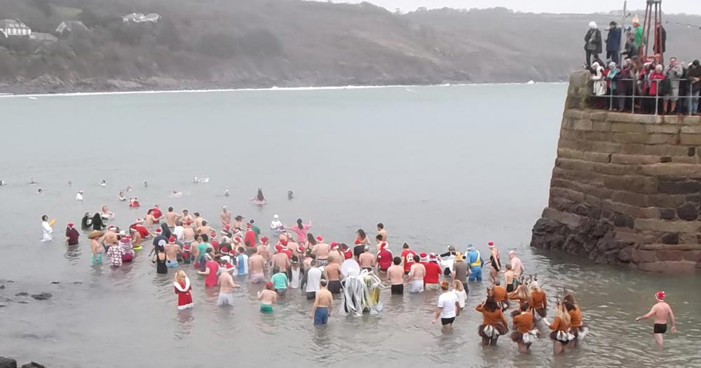 Large group of people in festive hats going for a sea swim in Cornwall on a misty day.