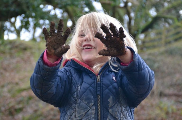 Child smiling and showing the camera her muddy hands as she plays at Bosinver.
