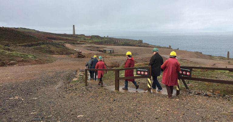 Six people in hard hats exploring Geevor Tin mine together during a grey and wet day.