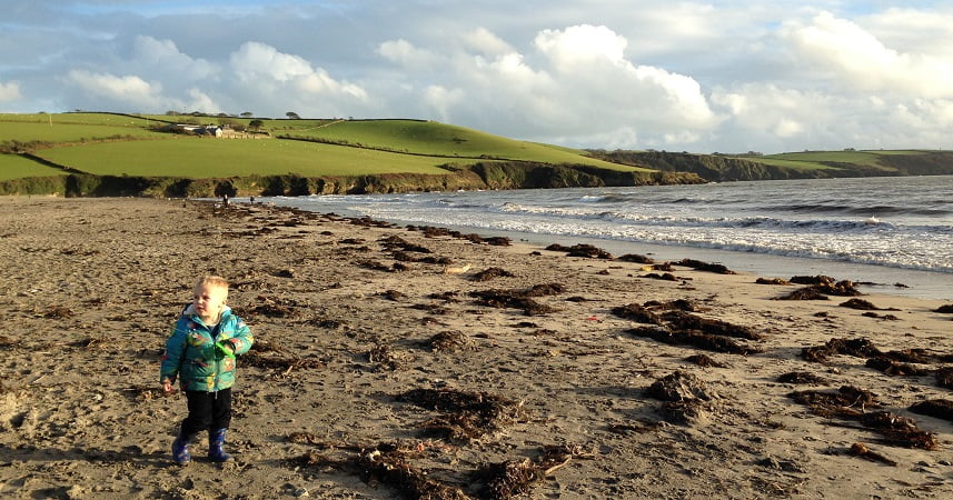 Child on a beach at Par Sands with the rollings hills and clouds in the sky in the background.
