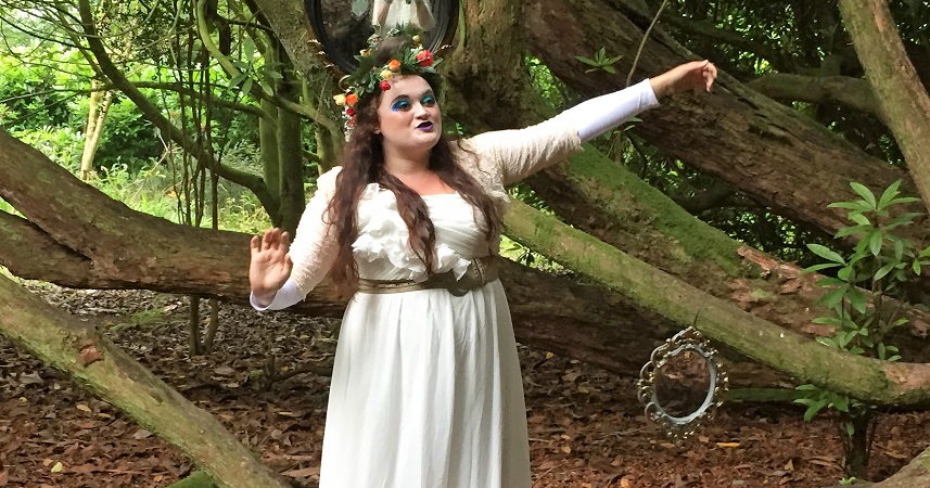 Female performer from the Rogue Theatre wearing a white dress and face make up whilst performing in Tehidy woods