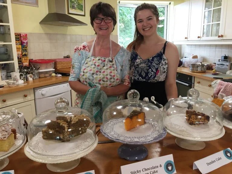 Mother and daughter proudly standing behind the goods they have baked together in a kitchen.