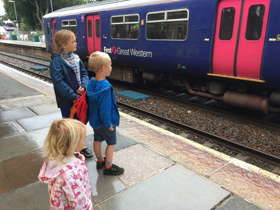Three children waiting patiently for a train at the train station.