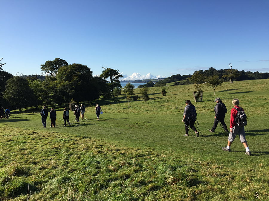 A group of walkers walking across a field to the Fal River, with the Fal river in the background.