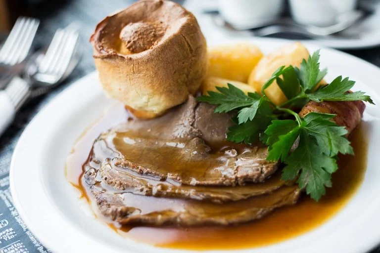Close up of Sunday lunch, including Yorkshire pudding, potatoes, beef and gravy.