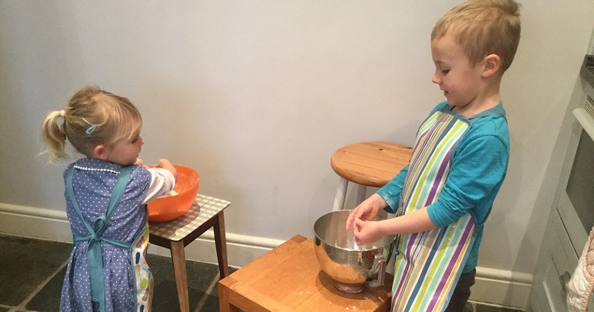A young girl and boy wearing stripey aprons, mixing ingredients in bowls