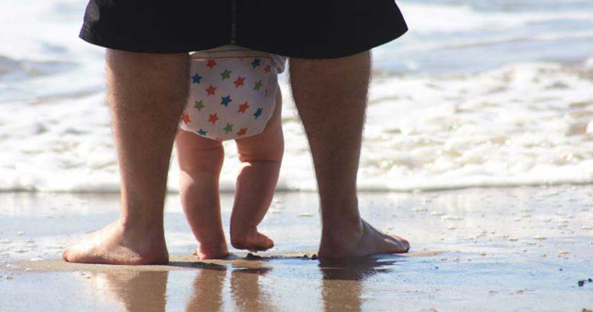 Close up shot of babys feet and parents feet on the beach with a wave about to come in
