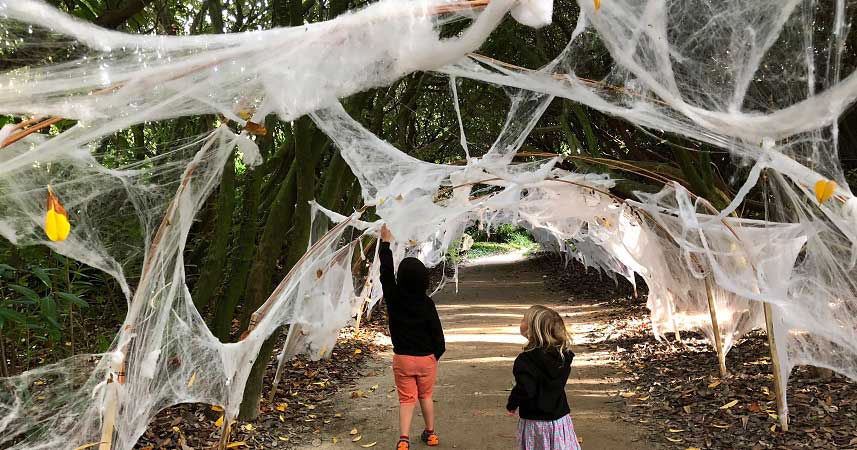Two small children walking through an archway of fake spider webs